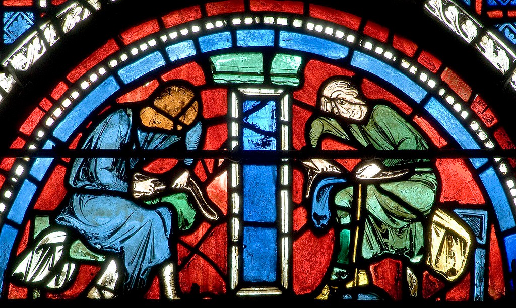 A close-up photo of a window displaying two men making shoes on their laps.