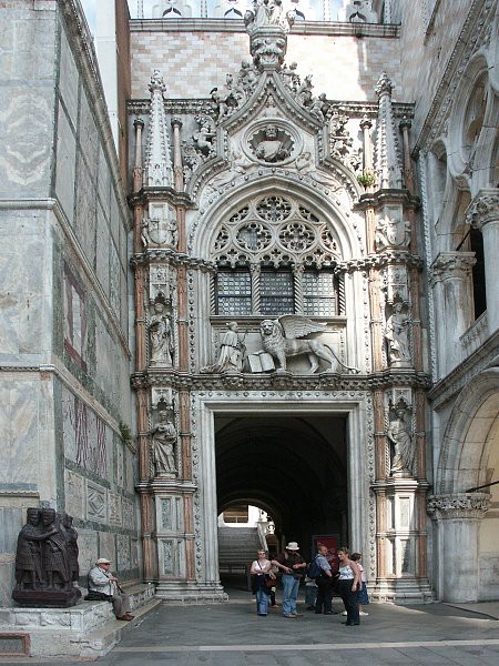 A photo of the Sculpture of four tetrarchs. Two pairs hug each other. It sits in front of a door of the wall of Saint Mark’s Basilica.