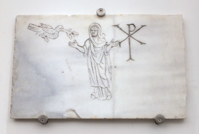 A marble slab with a robed man, a dove bringing him an olive branch and the initials Rho and Chi one on top of the other.