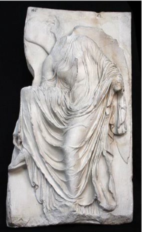 A photo of a bas relief depicting a now headless Athena adjusting her sandal. Her clothing is intricately carved, revealing her body underneath.