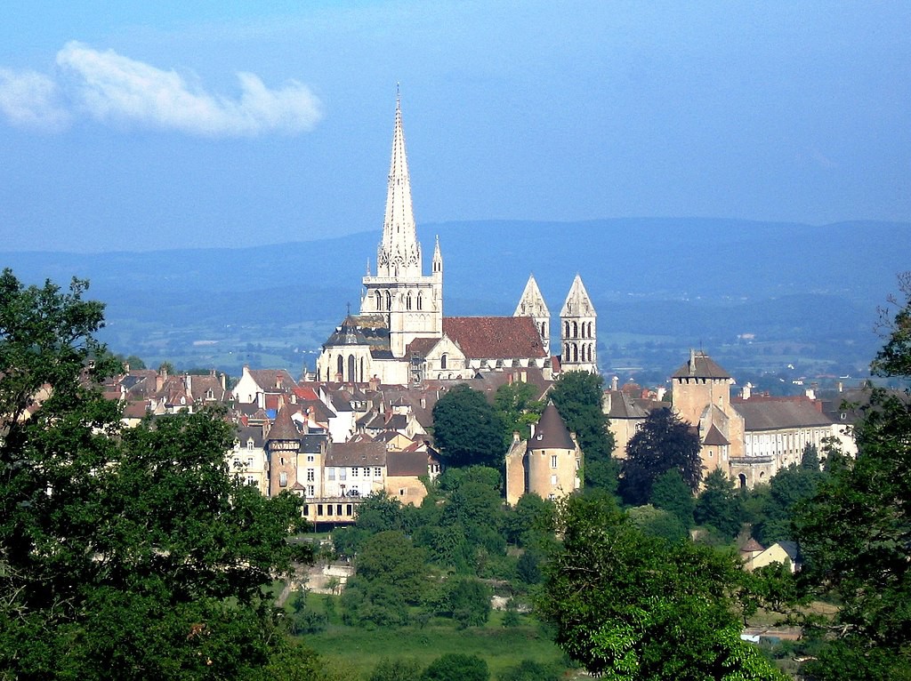 Distant view of a church with a tall white tower, two smaller white towers and red roof.