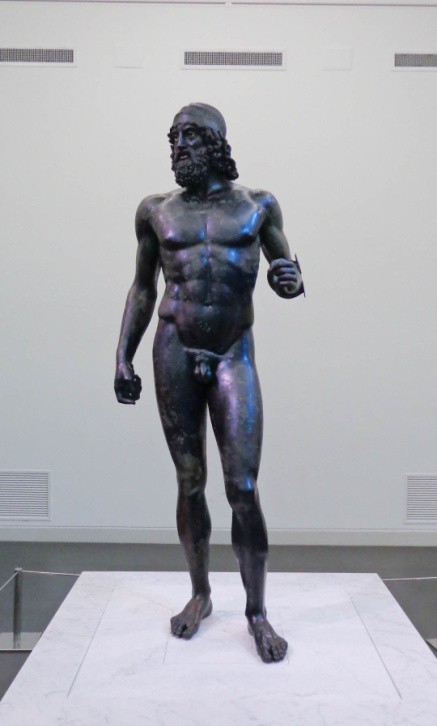 Full idealized figure of a bronze, bearded, nude warrior. His position indicates that he once held a spear.