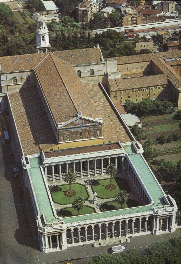 A bird’s eye view of Saint Paul’s. There is an enclosed courtyard with four areas of grass. A tree is in the center of each, and a statue stands in the center of the walkway separating the areas. Colonnades support the exterior of the courtyard as well as the entrance to the narthex.