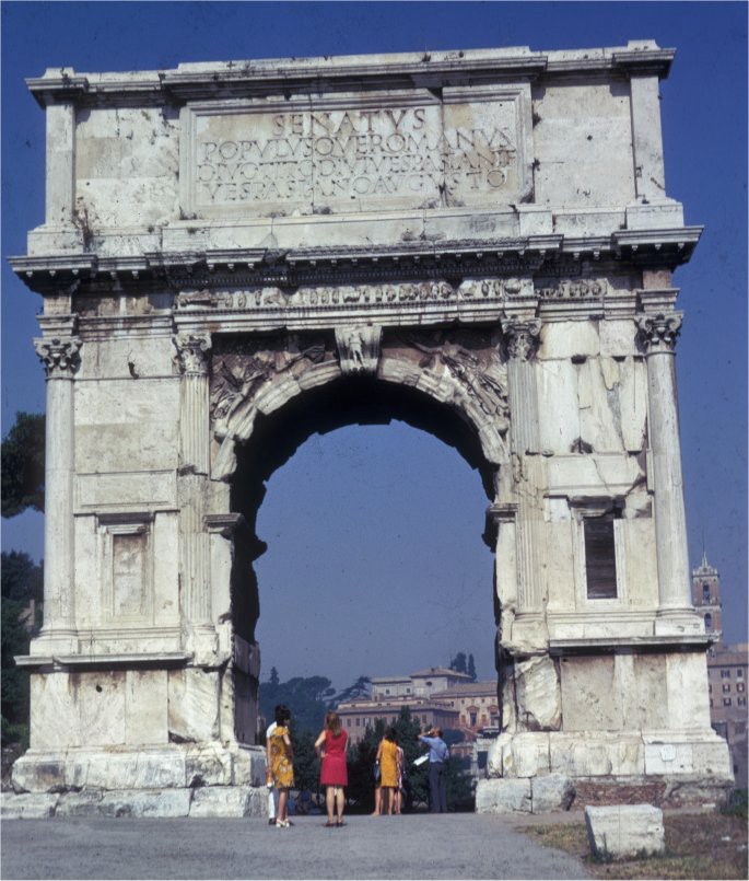 A large marble arch with a road passing through it. The arch is elaborately carved.