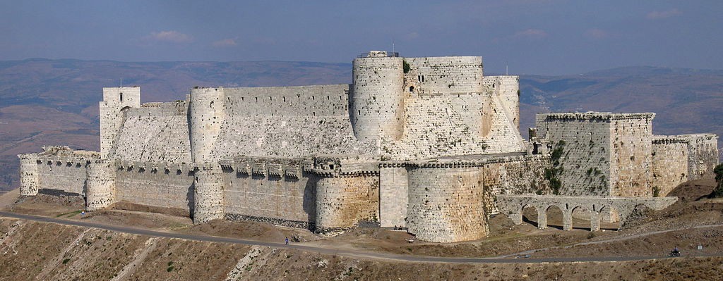 A photo of a large white castle with vegetation growing on its heavy walls.