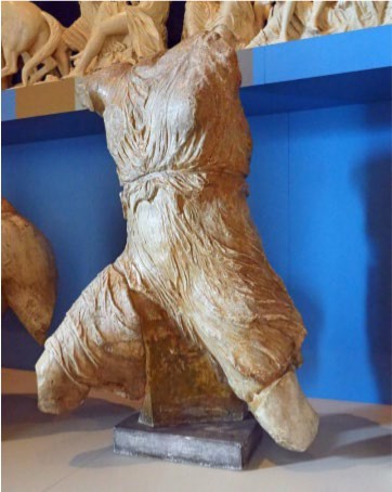 A photo of a damaged statue of Iris. The figure is active, and the clothing seems to blow in a wind.