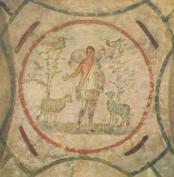 A ceiling fresco of a circle. In the center is a young man with a sheep over his shoulders and a sheep on each side. There is also a tree with a bird on each side behind the sheep.