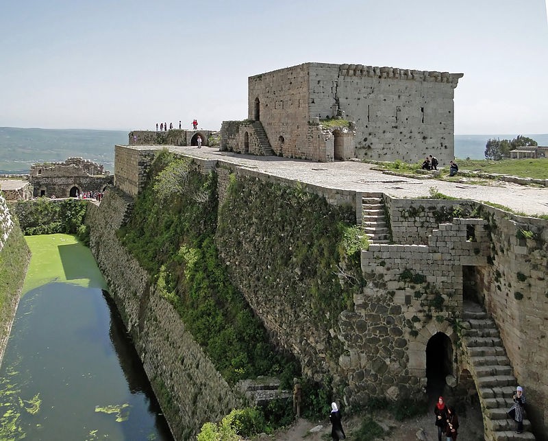 A view of the castle that includes water in a ditch beside the building but within the walls of the castle.