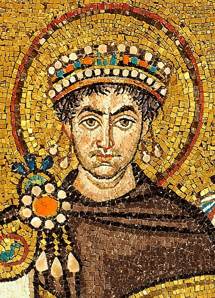 A close-up of Justinian’s head. He has a halo and wears a jeweled crown. He has an elaborate brooch and either wears earrings or has pearls hanging from his crown.