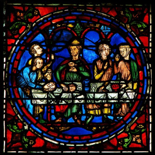 Jesus sits at a table with other guests holding a wine chalice.