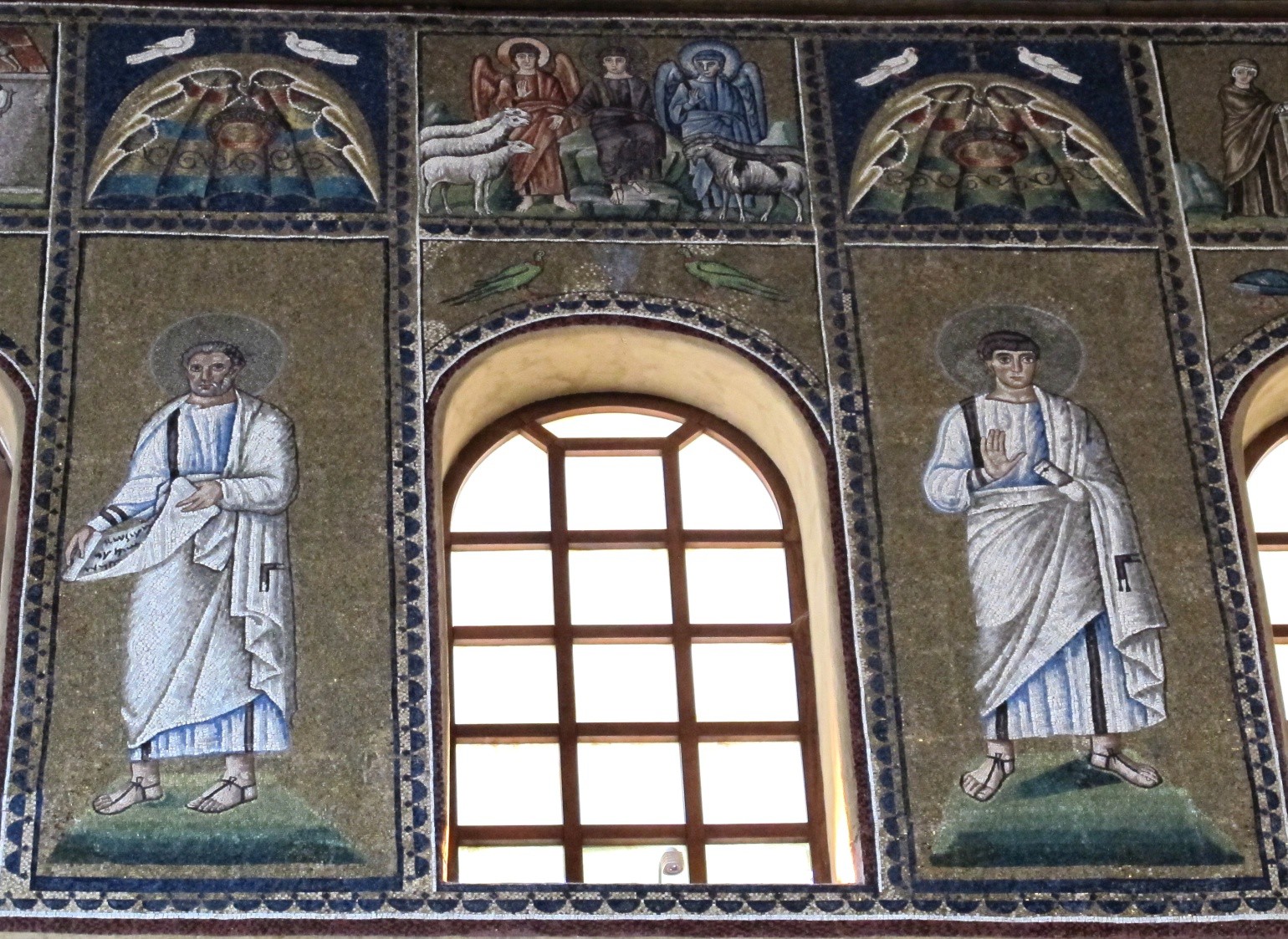 A large saint stands on each side of a window, which is divided into sections but is clear. Above the window is a smaller mosaic of Christ in a purple robe flanked by angels and separating sheep from goats.