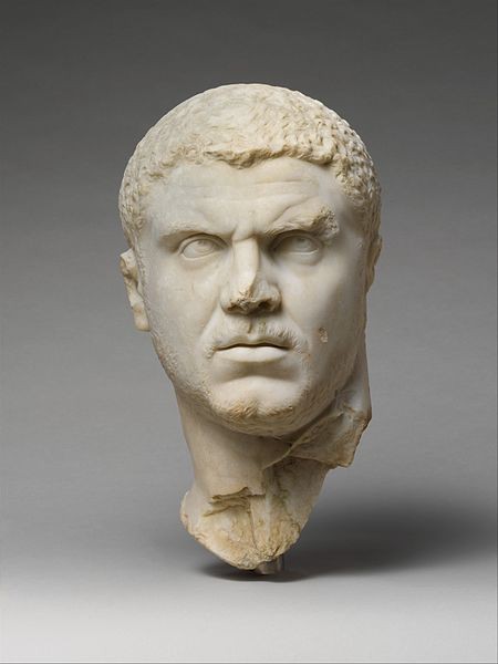 The carved marble head of an angry looking man with close-cropped hair. He needs a shave and has large, deep-set eyes.