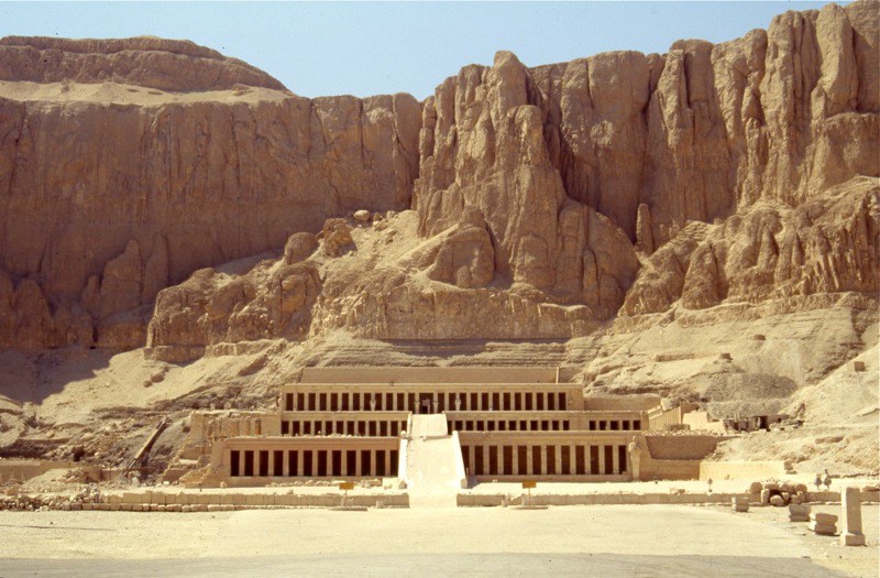 Front view of the elaborate temple of Hatshepsut. Only a few large statues remain in front of the square pillars that hold up the three stacked levels of the building, which is built into the side of the hill.