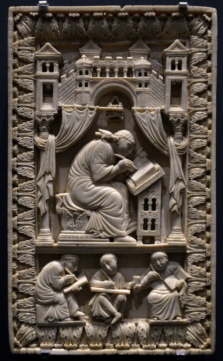 A carving in bas relief of monks writing, one at a desk and three on their laps.