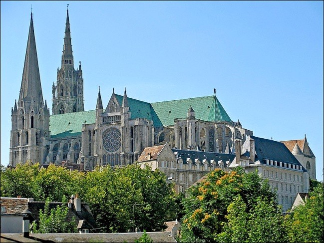 A southern view of Chartres with trees and bushes in front of it.