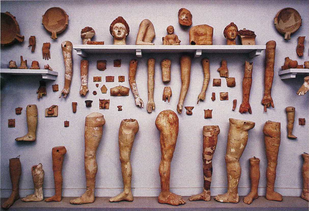 A photo of carved human limbs and other body parts, hanging or leaning against a wall.