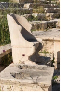 A marble seat with a back among the simpler flat stone seating that was later added by the Romans in the theatron.