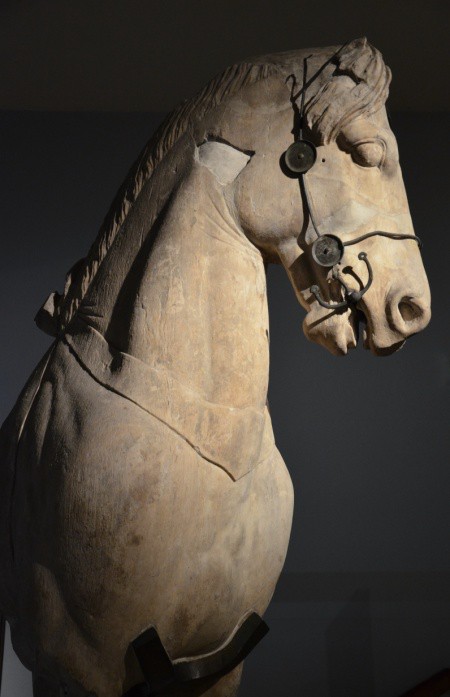 The sculptured head and neck of a horse with a metal bridle and bit.