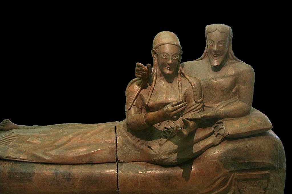 A sarcophagus decorated by two life-sized figures who smile as they recline. They closely resemble the Greek Archaic style and probably influenced it. The figures have braided hair and the male has a carefully groomed beard and powerful torso