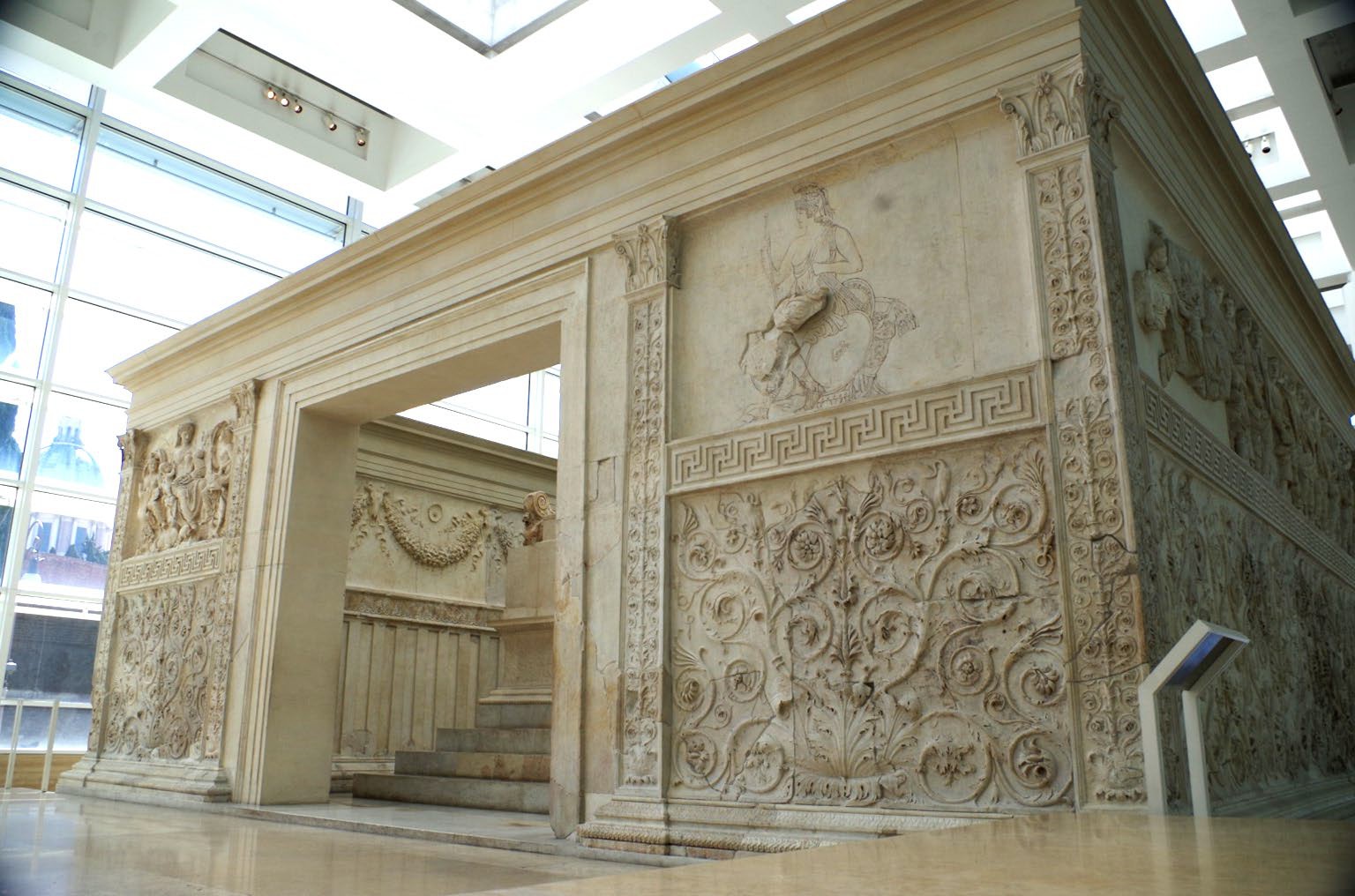 A small rectangular building with no roof and an open doorway. Inside there are steps visible and the outside is covered with carvings.