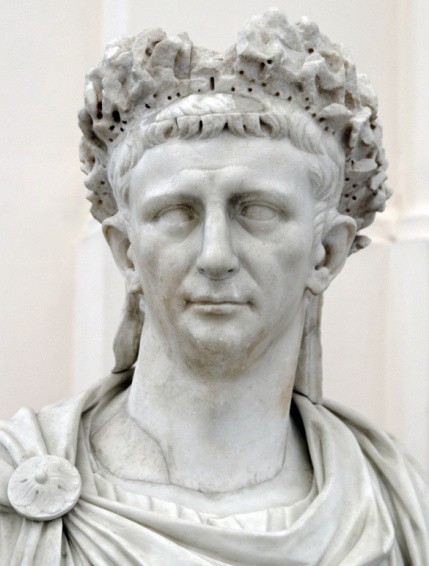 A white marble statue of a man with a receding chin and large ears, wearing a civic crown of leaves.