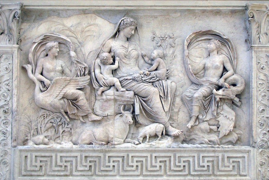 A bas relief of a woman with two babes in her lap. On each side of her sits a woman. One rides a swan and the other rides a dragon. Tiny cattle and sheep are at the mother’s feet.
