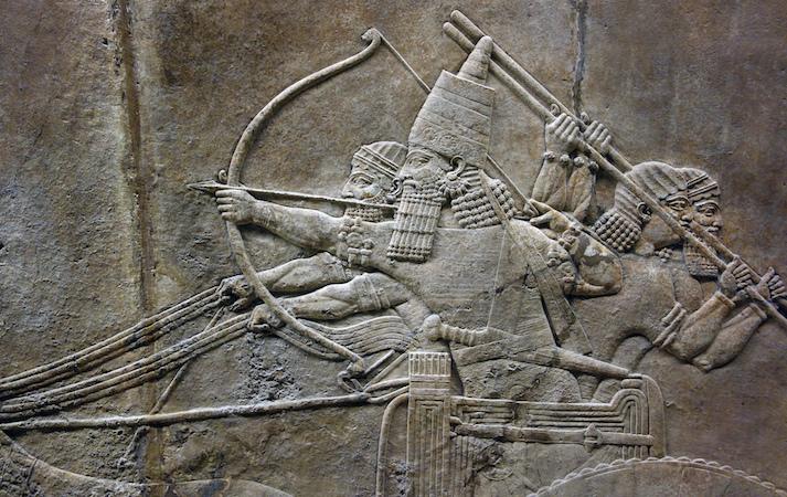 The king’s chariot pursues a lion while his men fend off another that attacks from the rear.