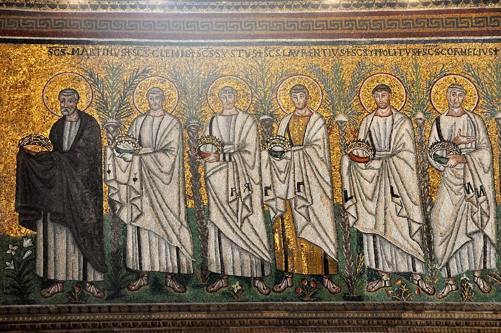 Close-up of a procession of men in white holding crowns.