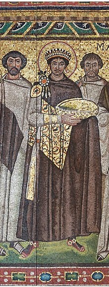 A piece of a mosaic presenting the Emperor Justinian with a crown and halo. He holds bread for the Sacrifice at the altar. Behind him stands his retinue.
