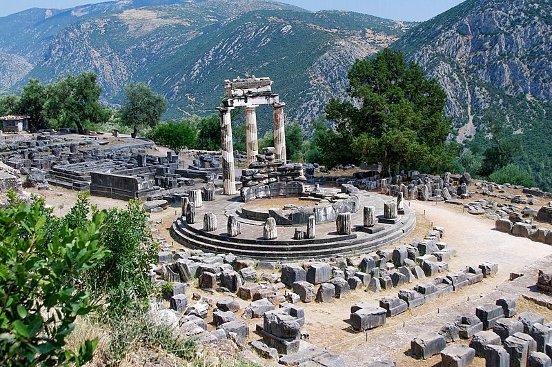 The ruins of a round Greek temple with a section of three pillars standing.