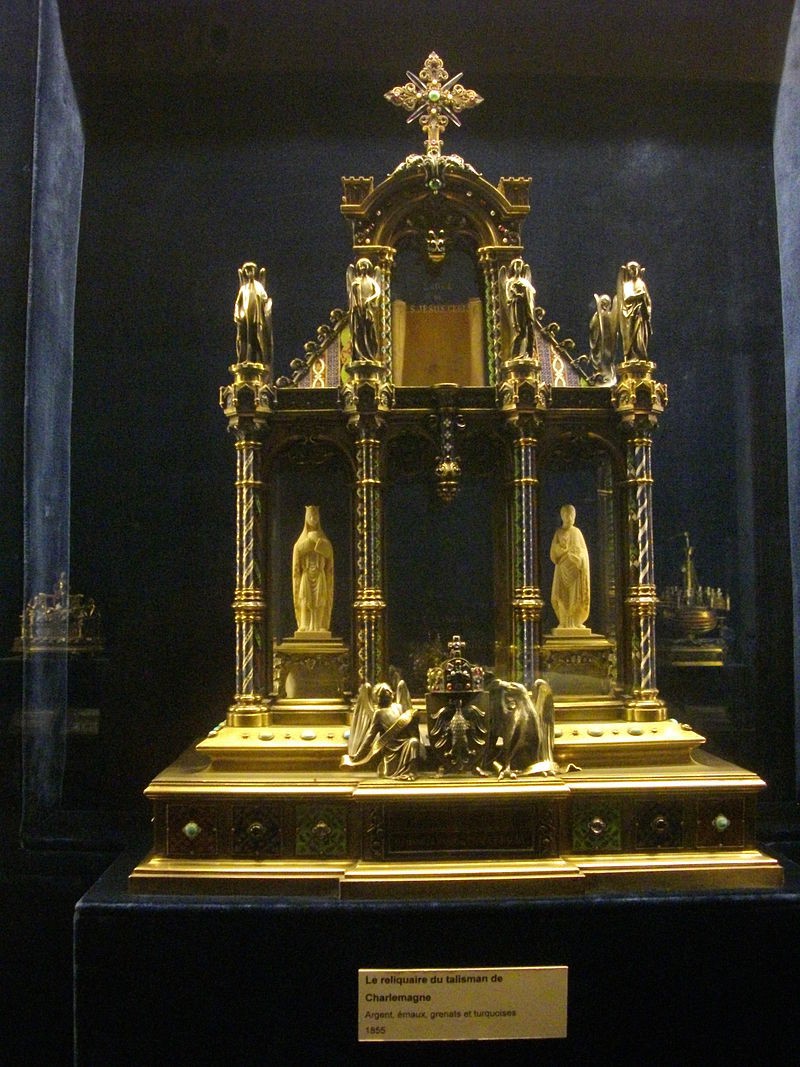 A reliquary shaped like a cathedral is made of gold. Four pillars support four angels, and an upper tower topped with a cross.