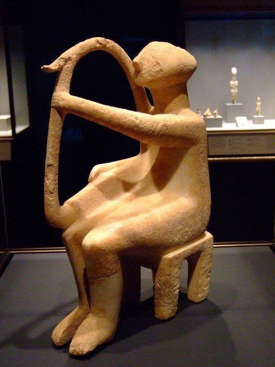 A simplified stone carving of a seated male playing a large harp.