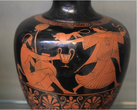 An image from a red figure pot. It shows a seated, nude satyr offering a drink to a follower of Dionysus. She has a small lion on her arm and her dress flows as she dances away.