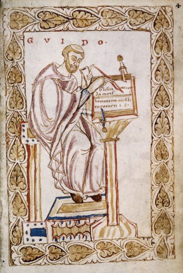 A monk sitting at a desk and writing with a quill pen.