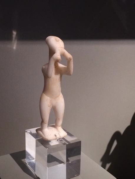 A simplified standing white stone figure playing a double flute.