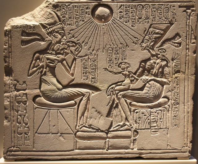 A carved block, probably from a wall depicting Akhenaten breathing life into his child while his wife holds his other daughter in her lap. Hands reach toward the couple from the rays of the sun.