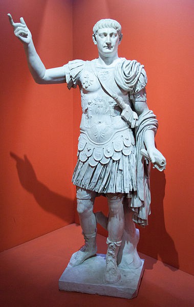 A while marble statue of a young man standing in a prima porta pose. He wears clothing as if going into battle.