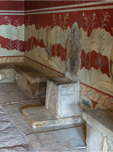 A stone chair and stone benches sitting next to a red and white fresco of foliage and exotic animals.