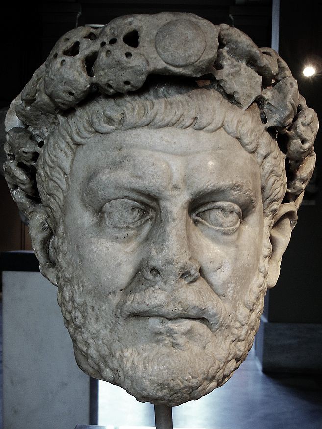 A damaged, marble head of a bearded man with close-cropped hair and a crown.