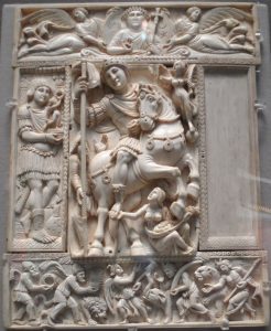 A bas relief of a large man riding a small horse. A tiny woman is at the feet of the animal. A beardless Christ is in the panel above the horseman. Refer to the text for details.