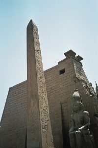 A stone temple with an obelisk and Egyptian statue in front of it.