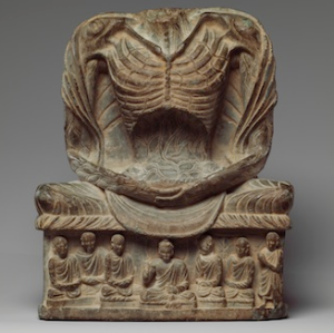 A carving of an emaciated torso seated with crossed legs on a raised platform. The front of the platform has small people surrounding a central figure. All are seated with crossed legs.