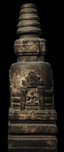 A solid stone stupa. There is a gate carved into it with a man seated inside with his legs crossed.