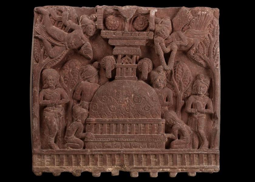 A stone carving of a stupa with people or gods around and above it.