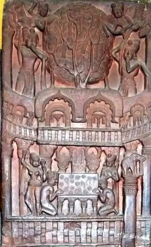 A solid stone stupa. There is a gate carved into it with a man seated inside with his legs crossed.