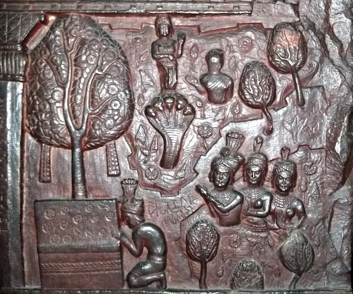 A carving of people worshipping an empty throne while surrounded by cobras, gods and trees. A tree seems to grow from the throne.